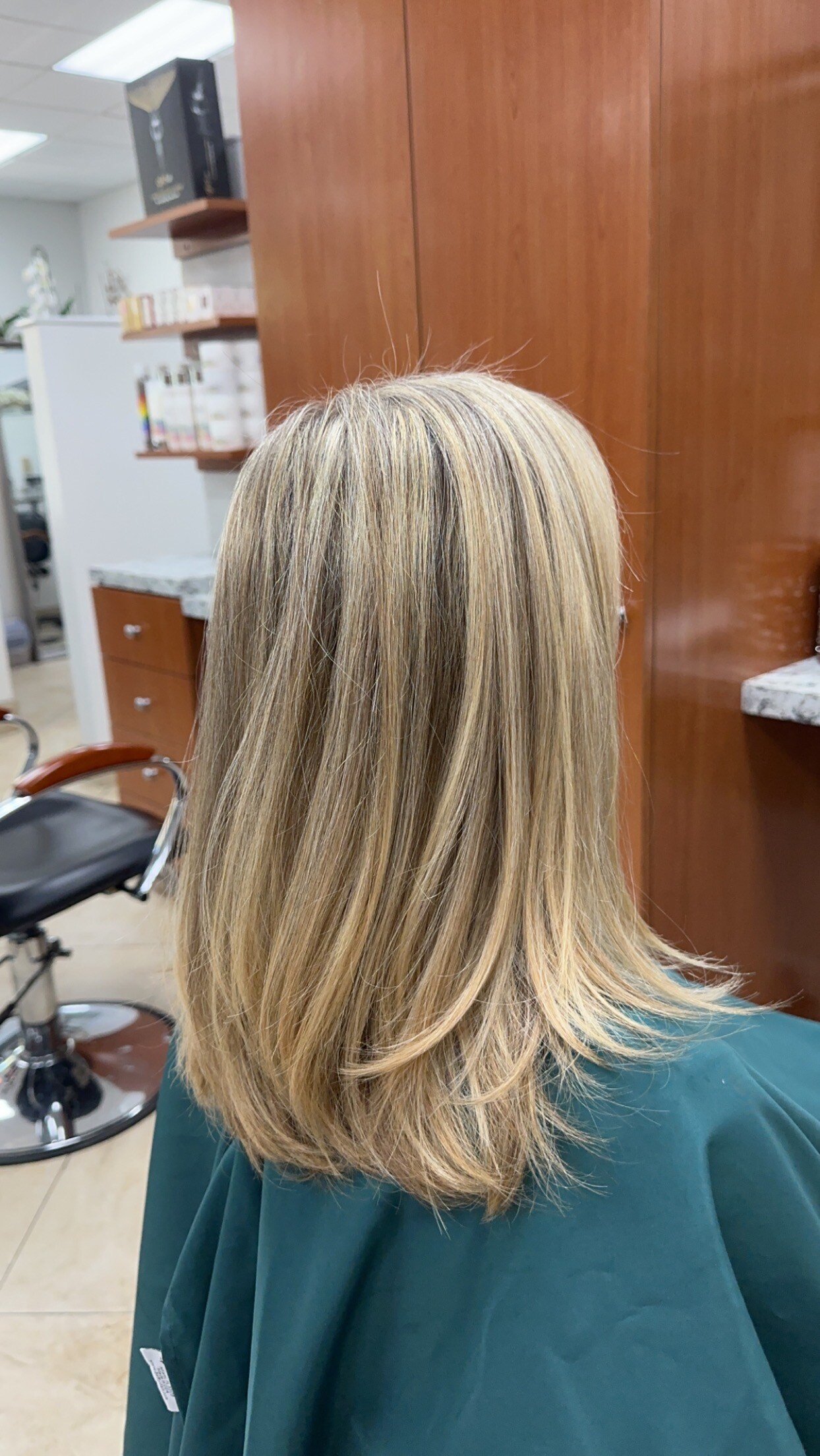 “Medium-length blonde hair with soft layers and highlights, styled in a sleek finish, photographed in a modern salon.”