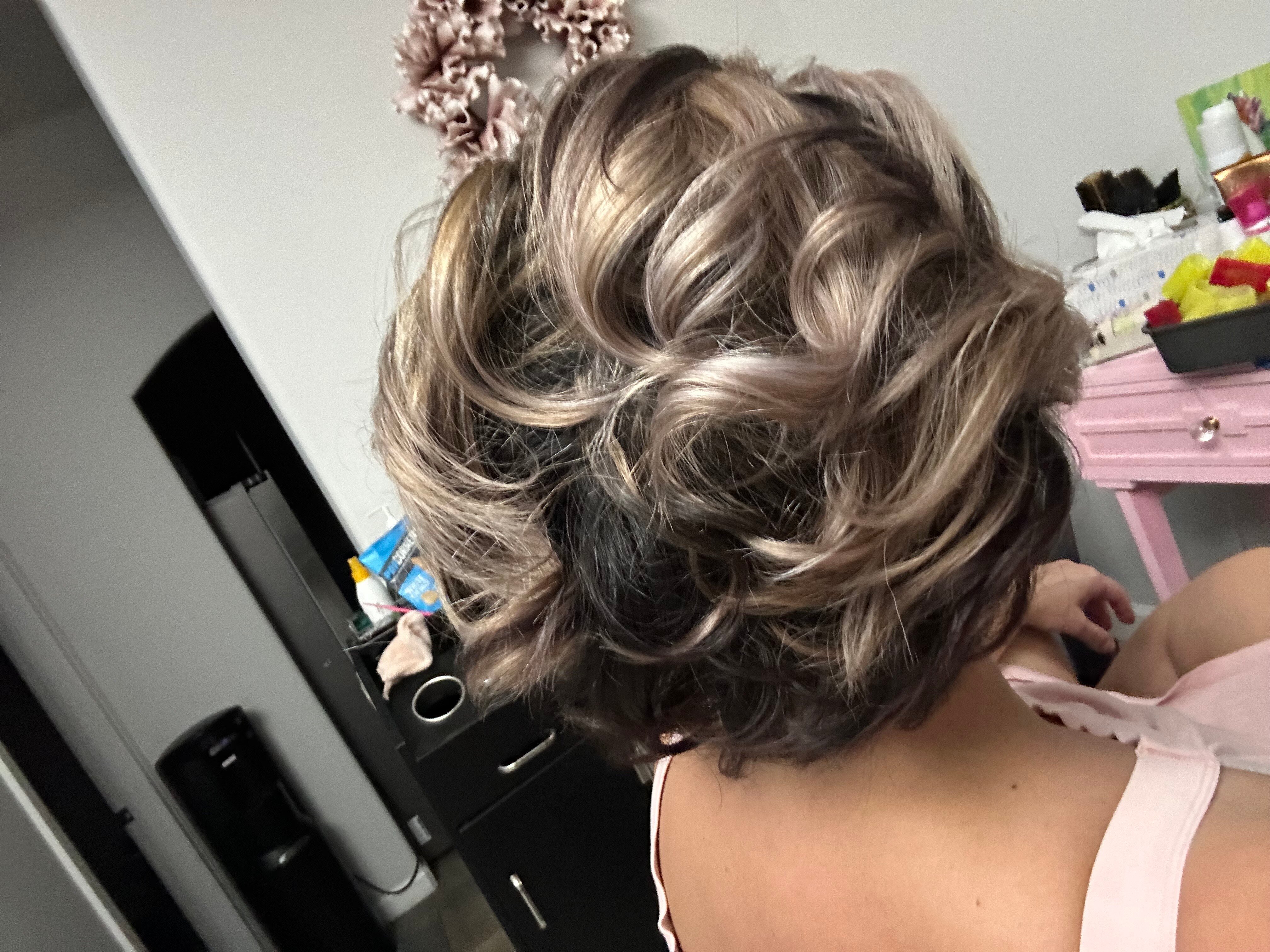 “Short, wavy hair styled with voluminous curls and blonde highlights, showcasing a professional salon finish.”